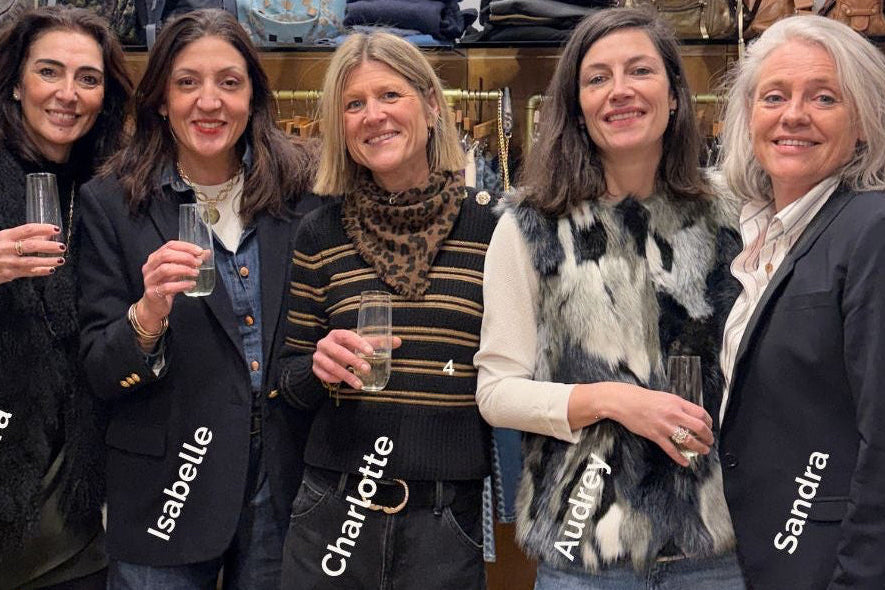 Five women standing together in a store with handbags displayed in the background.
